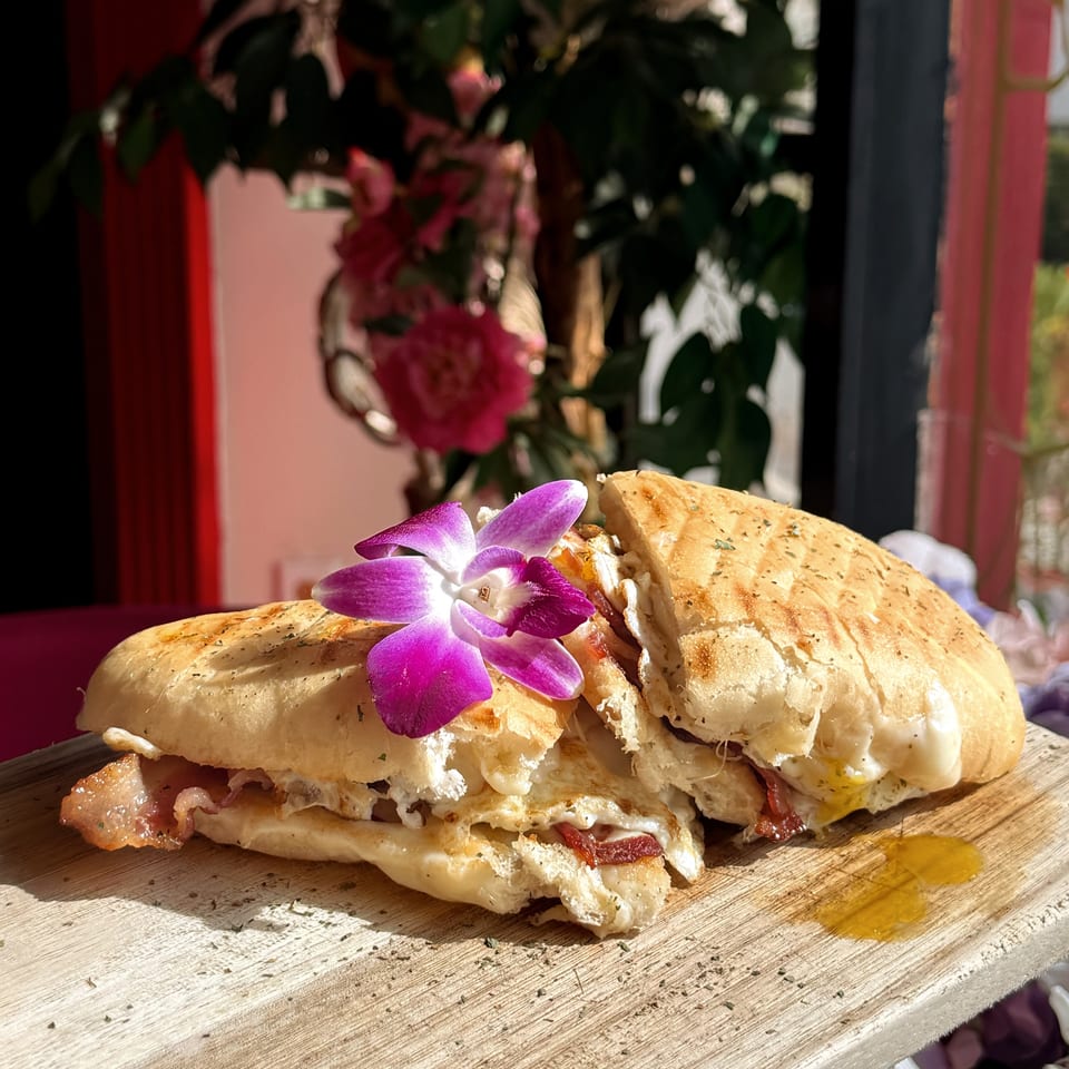 Toasted sandwich filled with melted cheese and bacon, garnished with a purple orchid on a rustic wooden table.