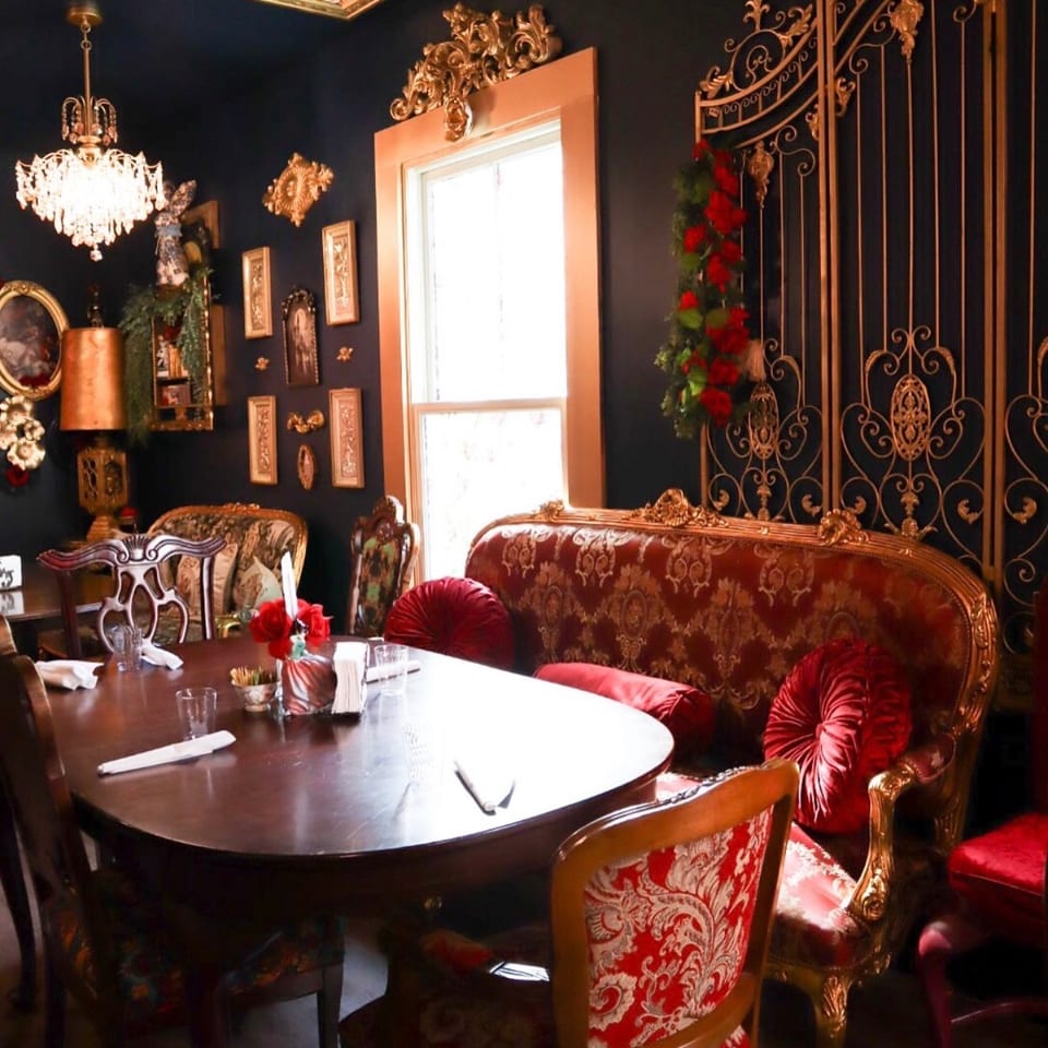 Ornate restaurant dining room with red velvet seating, gilded chairs, a decorated ceiling, chandelier, and formal table settings.
