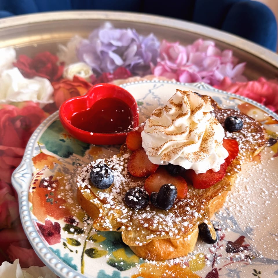 Dessert plate featuring powdered-sugar waffles, berries, whipped cream, fruit, and red dipping sauce on a floral dish.