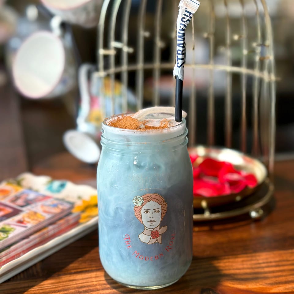 Blue iced drink in a branded glass jar, topped with cinnamon and a black straw, sits on a wooden restaurant table.